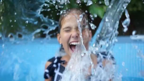 Близко красивый портрет девочки-подростка под потоком чистой воды. Девушку облили водой, она смеется и падает на спину в бассейн прямо в одежде — стоковое видео