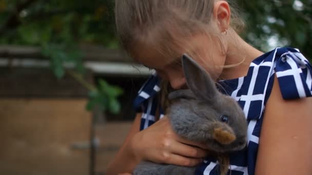 Buona infanzia. Chiudi il ritratto di una ragazza con un coniglio. Il bambino abbraccia delicatamente un coniglio grigio soffice, fattoria di coniglio — Video Stock