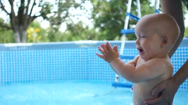 Feliz bebé de un año en la piscina aplaude en el verano y sopla burbujas. Feliz infancia. — Vídeo de stock