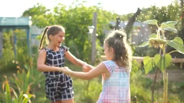 Děvčata se pod sprejem, která vede z hadice, točí rukama. Letní prázdniny, šťastné dětství — Stock video