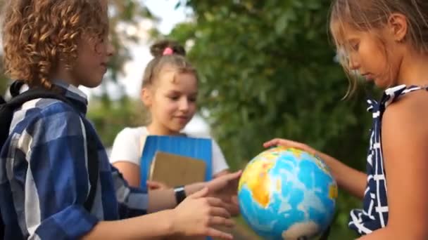 As crianças em idade escolar estão a considerar um grande globo. Retrato ao ar livre. De volta à escola, aulas de geografia, sonhos de infância de viajar — Vídeo de Stock