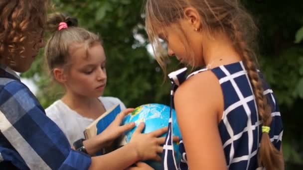 Due ragazze e un ragazzo, amici stanno considerando un grande globo mentre in piedi nel cortile della scuola. Ritorno a scuola, vacanze estive, vacanze scolastiche — Video Stock