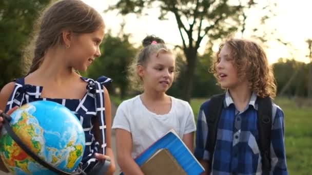 Мальчик и две девочки ходят в школу в пригороде и веселятся, разговаривая о чем-то, вернуться в школу, счастливые дети — стоковое видео
