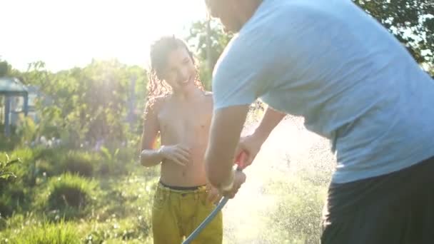 Fathers day. A man enjoys a summer vacation with his son, father and son water each other from a hose Stock Video