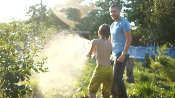 Mann genießt Sommerurlaub mit seinem Sohn, Vater und Sohn gießen sich gegenseitig aus einem Schlauch. Vatertag — Stockvideo