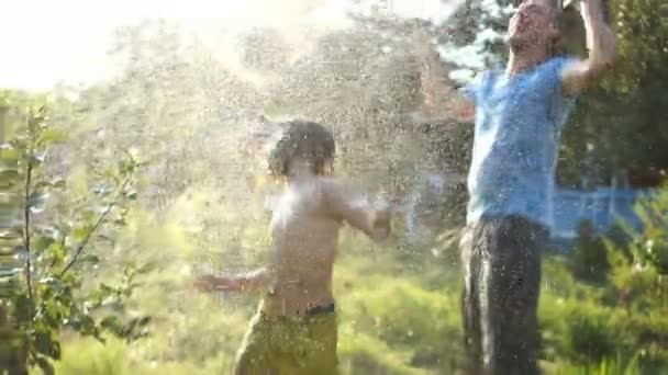 Padre e hijo jugueteando regándose unos a otros de una manguera en un caluroso día de verano. Vacaciones en el campo, vacaciones de verano — Vídeo de stock