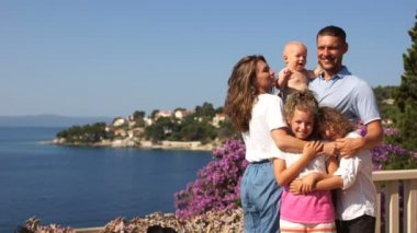 Deniz terası, çocuklu ebeveynler, çocuklu tatiller, yaz tatilleri. Üç çocuklu mutlu bir aile Akdeniz'deki bir tatil beldesinde dinleşiyor.