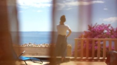 Güneşli bir terasta güzel genç bir kadın. Perdearkasından arka görüş. Sahil beldesi, kadınlar günü