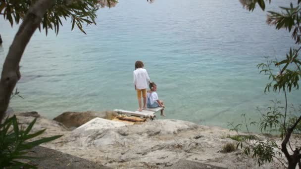 Подростки, мальчик и девочка сидят на берегу моря. Летние каникулы, отдых в экзотических странах — стоковое видео
