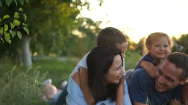 村の草の上で横たわって3人の子供を持つ幸せな若い家族。夏休み、家族の日 — ストック動画