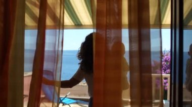 Kollarında bebek olan bir kadın, deniz manzaralı güneşli bir terasta duruyor. Resort Mülkiyet, Aile Hafta sonu, Anne ve Çocuk