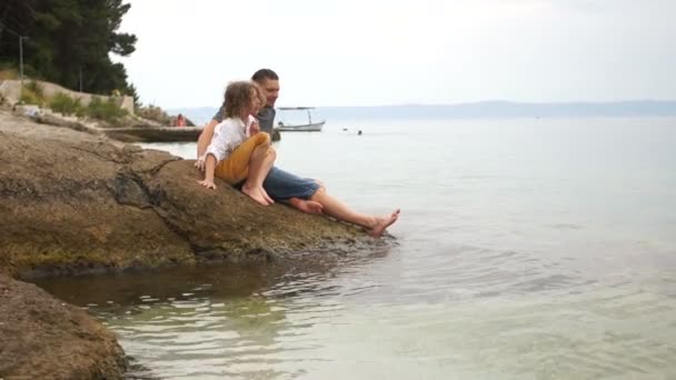 Far och son slappnar av tillsammans på en stenig strand. Tal om far och son, vuxen man och Lille pojke. Pappas dag — Stockvideo