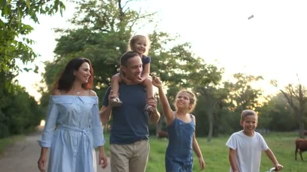 Прекрасна молода щаслива родина на прогулянці. Чоловік і дружина і троє дітей ходять по дорозі в селі на заході сонця. Літні канікули — стокове відео