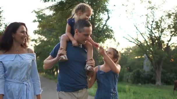 Mann und Frau mit ihren Kindern spazieren gehen. Ein kleines Mädchen sitzt auf den Schultern ihres Vaters. glücklicher Familienurlaub — Stockvideo