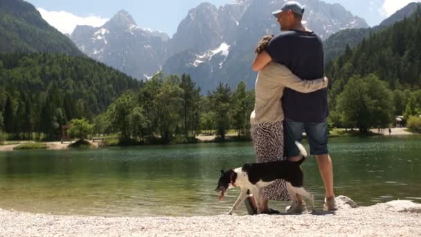 Liefdevolle echtpaar rustend op de oever van een prachtig bergmeer. Een man en een meisje bewonderen het prachtige berglandschap. Gelukkige familie vakantie — Stockvideo