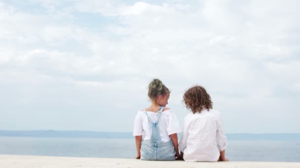 Το αγαπημένο αγόρι και κορίτσι που κάθονται στην παραλία αγκαλιάζοντας. Ημέρα του Αγίου Βαλεντίνου, καλοκαιρινές διακοπές, έφηβοι πρώτη αγάπη — Αρχείο Βίντεο