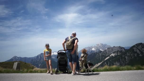Rodzice i troje dzieci. Rodzina z małym dzieckiem w spacerze cieszy się pięknym widokiem na góry z boku drogi. Nastolatek dziewczyna tańczy ze szczęściem przed kamerą — Wideo stockowe