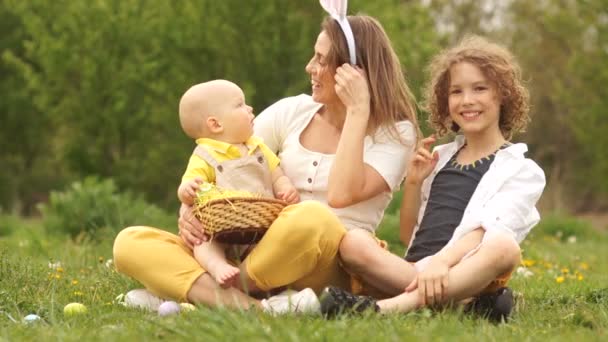 Vídeo engraçado família Páscoa feliz em um piquenique no parque. Mamãe coloca o bebê nos ouvidos do coelho da Páscoa — Vídeo de Stock
