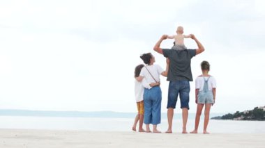 Anne ve baba ve üç çocuğu beyaz kum üzerinde deniz kıyısında durmak. Kot pantolon giymiş aile, mutlu aile tatili