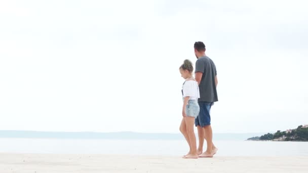Młody mężczyzna i dwoje dzieci, chłopiec i dziewczynka, siedzą na białym piasku nad morzem. Urlop letni, dzień ojców — Wideo stockowe
