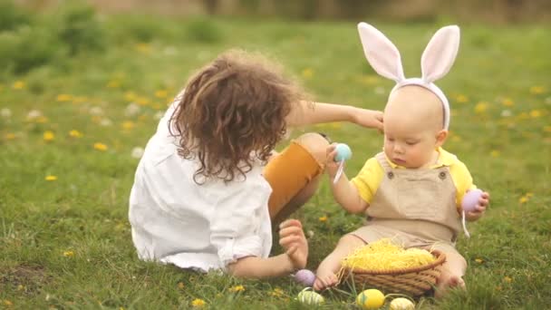 Милые дети, школьник и ребенок, играют с пасхальными яйцами, сидя на зеленой траве. Пасхальная корзина — стоковое видео
