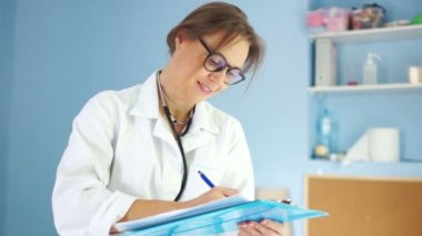 Beyaz bir tıbbi ceket ve bir fonndoskop ile Lovely kadın doktor çerçeve içine bakar ve beyaz dişli bir gülümseme ile gülümsüyor. Uluslararası Doktor Günü