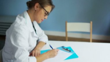 Gözlükgüzel kadın doktor hastaların tıbbi geçmişi doldurur, ve sonra kameraya bakarak ve gülümseyerek. Sağlık ve tıp kavramı, uluslararası doktorlar günü