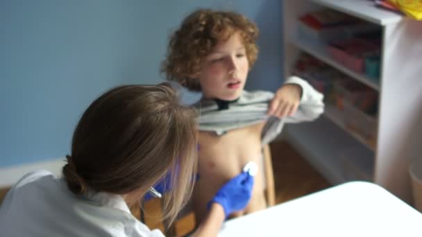 Le pédiatre écoute les poumons de l'enfant à l'aide d'un stéthoscope. Toux de garçon, gants bleus, journée internationale des médecins — Video