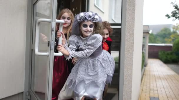 Děti v halloweenských kostýmech a make-upu vyběhnou ze vchodu do činžovního domu. Halloween tradice — Stock video