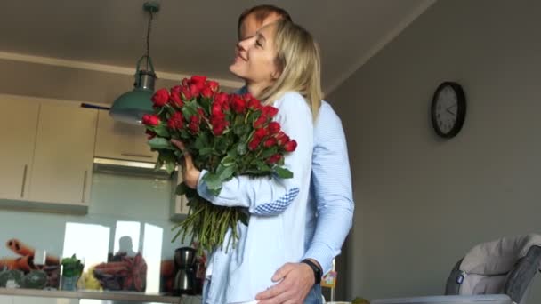 Boldog férj és feleség az otthonukban. Egy férfi nagy csokor vörös rózsát ad egy nőnek. Szeretők Valentin-napon — Stock videók