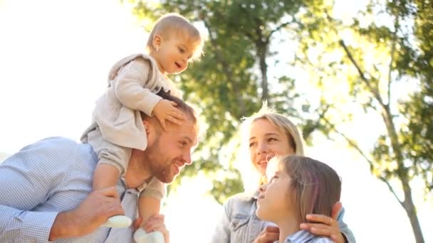 Par som ger två små barn piggyback rider leende. Glad familj som leker utomhus. Familjen njuter tillsammans i naturen — Stockvideo