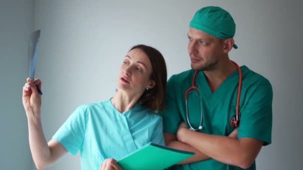 Dva doktoři, muž a žena, vyšetřují rentgenovou fotografii pacienta. Lékařský personál diskutovat X-ray výsledky — Stock video