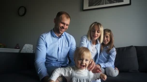 Sonrientes padres jóvenes con dos hijos en casa. Familia feliz de cuatro se divierten en casa en el dormitorio — Vídeos de Stock