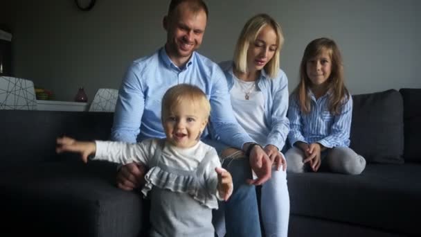 Unga föräldrar, man och hustru, och deras två döttrar är klädda i denim och ler glatt. Lycklig familj hemma på helgen — Stockvideo