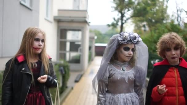 Los niños con disfraces de Halloween se divierten corriendo por la calle. Maquillaje sangriento, los escolares celebran Halloween — Vídeo de stock