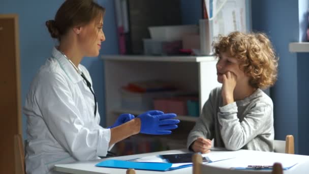 Ragazzo riccio adolescente ad un ricevimento dal pediatra. Medico femminile ascolta i polmoni e bronchi in un adolescente — Video Stock