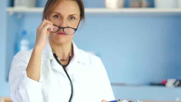 Eine seriöse Ärztin in weißem Mantel und Brille mit einem Ordner in der Hand an den Wänden des Büros. Medizin und Gesundheitskonzept — Stockvideo