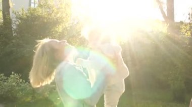 Mutlu anne kızıyla eğleniyor. Genç bir kadın bir yaşındaki bir çocuğu parktaki güneşin batışına fırlatıyor.