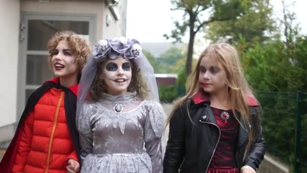 Счастливой прогулки на Хэллоуин. Дети в костюмах ведьмы, мертвой невесты и вампира ходят по улице — стоковое видео