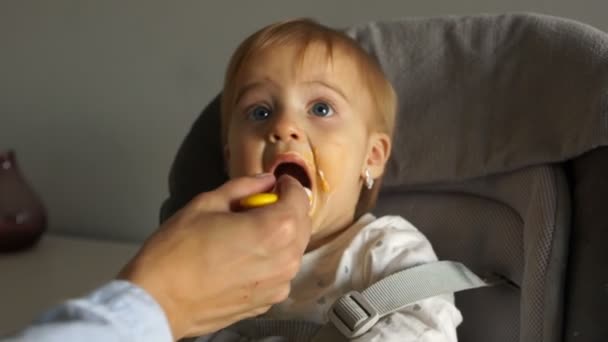 신원 미상의 엄마는 한 살짜리 딸에게 숟가락을 먹여. 어린이는 높은 의자에 앉는다. 유아들의 건강 한 식사 — 비디오