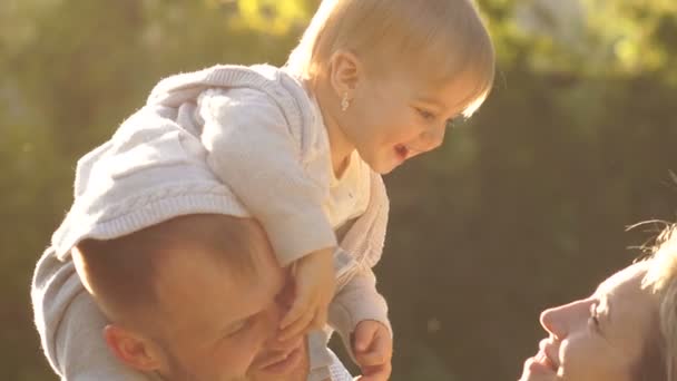 Feliz familia joven pasar tiempo juntos fuera. Retrato cercano de una hermosa familia feliz en el parque en los rayos del sol poniente — Vídeos de Stock