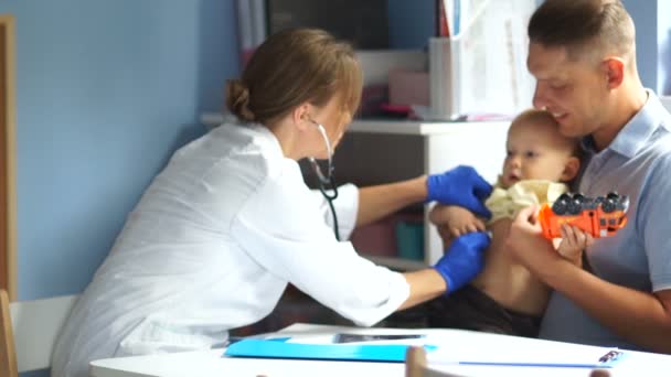 Vrouwelijke arts onderzoekt een kleine anderhalf jaar oude jongen. Vader en zijn baby bij een kinderarts afspraak. Vaderdag — Stockvideo