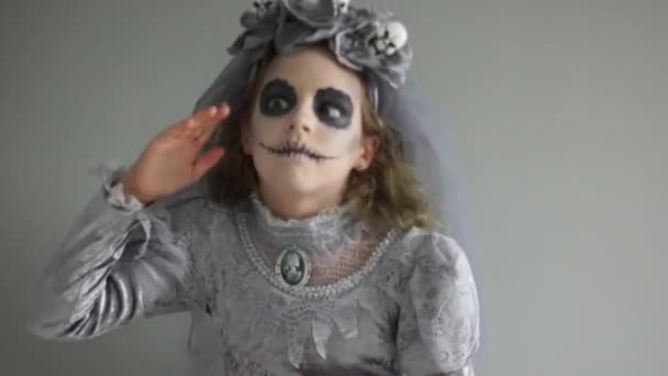 Празднование Хэллоуина. Близкий портрет красивой девочки-подростка в сером костюме и макияж мертвой невесты. Завеса с черепами — стоковое видео