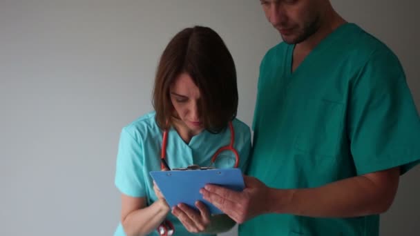 Femme médecin signe les documents dans un dossier entre les mains de son jeune stagiaire. Médecin et interne, assistant médical — Video