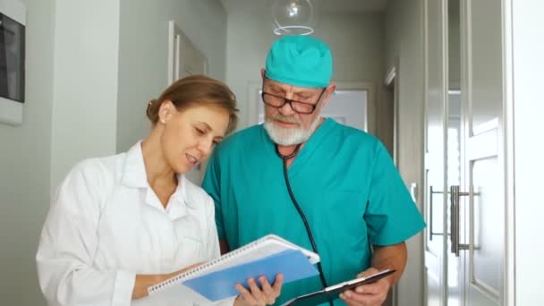 Δύο γιατροί, άνδρες και γυναίκες, μιλούν στο διάδρομο της κλινικής. Ιατρική έννοια υγειονομικής περίθαλψης — Αρχείο Βίντεο