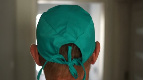 Les chirurgiens font un gros plan. Erreur médicale. Un homme en blouse médicale marche le long du couloir, s'assoit sur une chaise et enlève son chapeau.Chirurgien fatigué après l'opération — Video