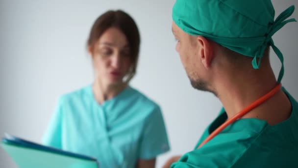 Sjukvårdspersonal på jobbet. Praktikanten och läkaren konsulterar i korridoren på kliniken. Kvinna och man i medicinska klänningar. Medicin och hälsovård — Stockvideo