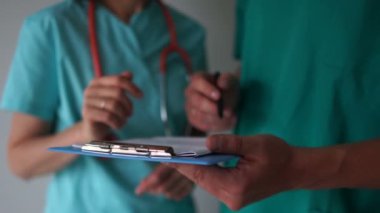 Doktorların el ve belgelerine yakın çekim. Doktor tıbbi belgeleri asistanının elinde imzalar.