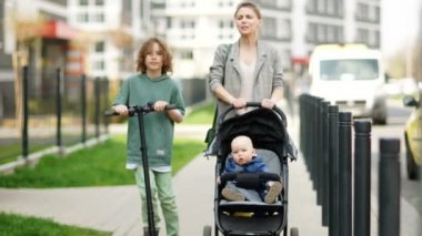 Oğullarıyla birlikte şehir caddesinde yürüyen bebek arabalı güzel genç bir kadın. Müstehcen okul çocuğu elektrikli scooter kullanıyor. Anneler Günü