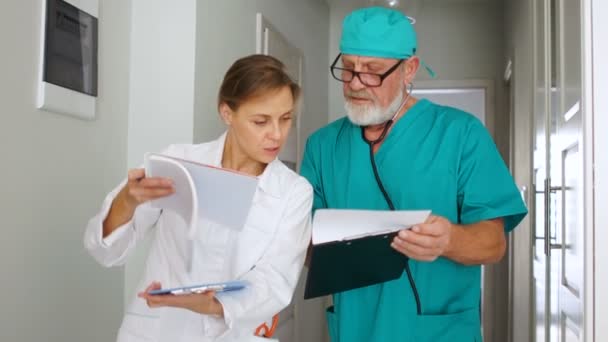 Medici di sesso maschile e femminile in tuta medica discutendo i risultati dei test dei pazienti nel corridoio della clinica — Video Stock